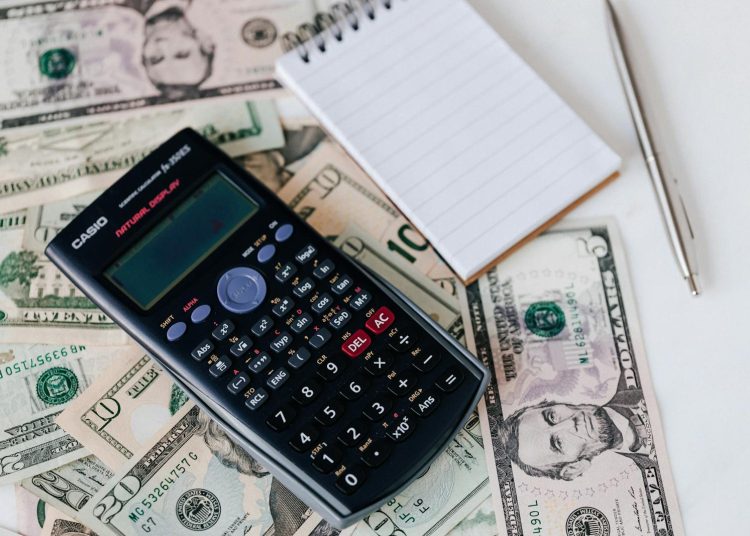 From above electronic calculator and notepad placed over United States dollar bills together with metallic pen for budget planning and calculation